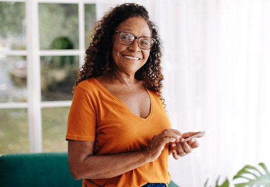 Senior woman with glasses smiling while looking at phone