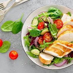 Bird’s eye view of a bowl of salad with chicken next to utensils