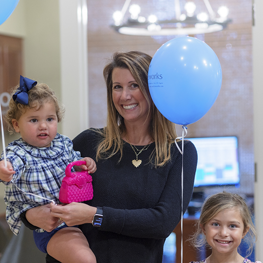 Smiling dental team member holding a toddler and balloons